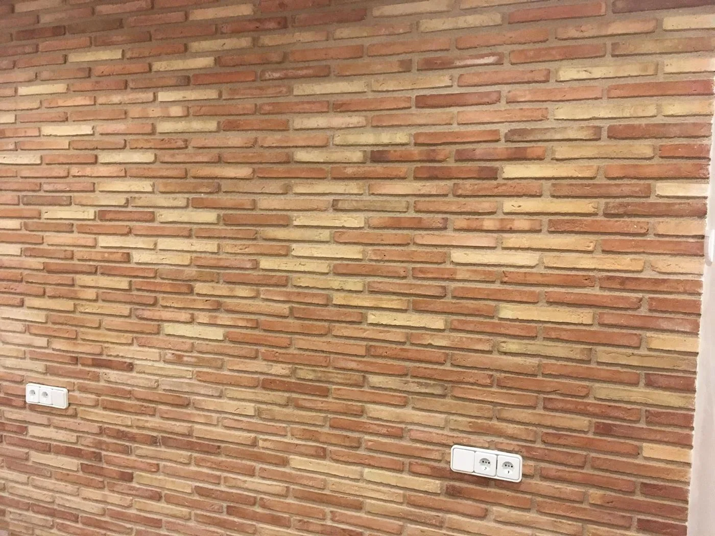 Paret de maó vist amb els tons barrejats de palla i roig
